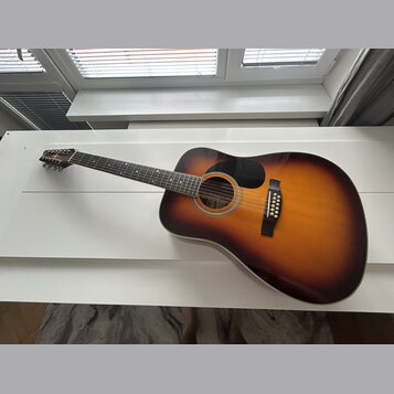 Akustická kytara s korpusem v barevném přechodu od žluté přes oranžovou k hnědé (sunburst). Na hmatníku jsou vidět bílé polohové značky a na hlavě ná…