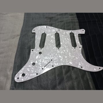 Bílý pickguard s perleťovým efektem určený pro elektrickou kytaru. Povrch je hladký a reflexní, bez viditelných značek, log nebo nápisů. Kousek vykaz…
