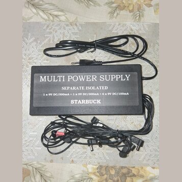 Černý napájecí adaptér s nápisem MULTI POWER SUPPLY, SEPARATE ISOLATED a STARBUCK. Pod názvem je uveden text 1 x 9V DC/500mA + 1 x 9V DC/300mA + 6 x…