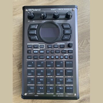 Černý sampler Roland SP-404MKII s digitálním displejem a ovládacími prvky. V horní části jsou čtyři otočné knoflíky s popisky VOLUME, CUTOFF, RESONAN…