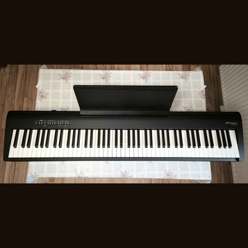 Černý digitální piano s bílými a černými klávesami a přiloženým notovým pultem. V pravém horním rohu je bílý nápis Roland FP30. V levé části horního…