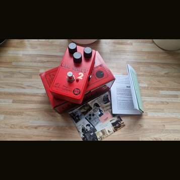 Červený kytarový efekt s třemi černými oválnými knoflíky. Na horní straně je nápis BIG MUFF a bílá číslice 2, níže se nachází logo electro-harmonix s…