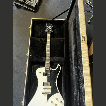 Bílá elektrická kytara s černým pickguardem v otevřeném kufru s černou vnitřní výstelkou. Na hlavě hmatníku je viditelné logo "Epiphone". Nástroj má…