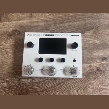 Bílý efektový procesor Hotone Ampero Stomp. Na horní hraně je nápis AMPERO STOMP, CDCM HD Gen 2 Amp Modeler / Effects Processor a logo HOTONE. Zaříze…