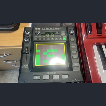 Černý syntezátor s nápisem KORG KAOSSILATOR PRO+ DYNAMIC PHRASE SYNTHESIZER / LOOP RECORDER. Zařízení má centrální dotykový displej s viditelnými škr…