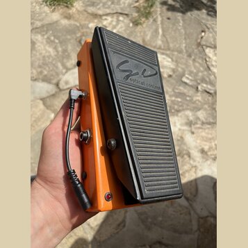 Oranžový expresní pedál s černým žebrovaným šlapadlem. Na horní části šlapadla je nápis „optical control“ a nad ním stylizovaný podpis. Na boku pedál…