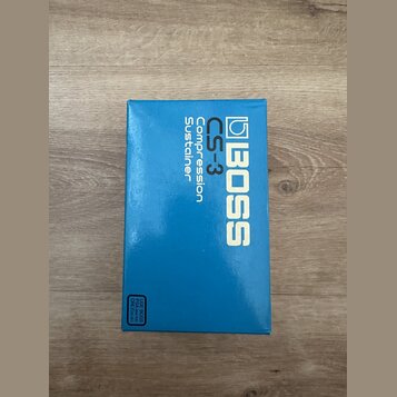 Modrá krabice od efekt pedálu s bílými nápisy. Na přední straně je logo BOSS a označení CS-3 Compression Sustainer. V levém dolním rohu je malý text…