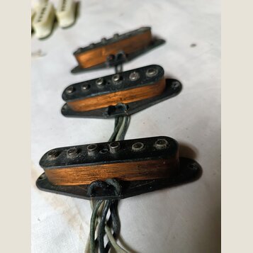 Tři elektrické snímače typu single-coil s oranžovými cívkami a černými plastovými základnami. Snímače mají kovové pólové šrouby a jsou připojeny k če…