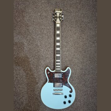 Světle modrá elektrická kytara s tmavým hmatníkem a vložkami z perleťového materiálu. Na těle je tmavě červený pickguard s texturou želvy a dva humbu…