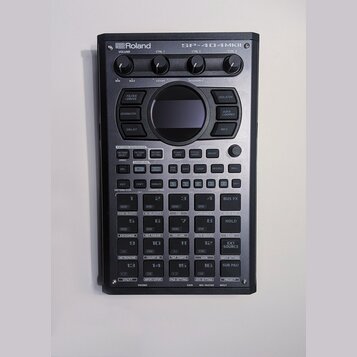 Černý sampler Roland SP-404MKII. Zařízení obsahuje několik otočných ovladačů, displej a mřížku 16 ovládacích padů. Povrch je v dobrém stavu bez vidit…