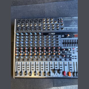 Míchací pult značky behringer, model XENYX X1822USB. Zařízení je v kovovém šasi s množstvím regulačních knoflíků, posuvníků a konektorů. Na horní čás…