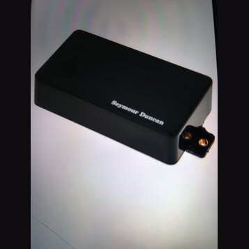 Černý obdélníkový box z plastu nebo kovu. Na horní straně je bílý nápis Seymour Duncan. Z pravého boku vyčnívá černý konektor se dvěma zlatými kontak…