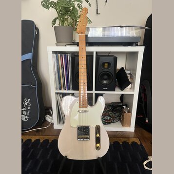Elektrická kytara typu Telecaster v krémové barvě s bílým pickguardem a světle hnědým hnedem hmatníkem. Na hlavě je viditelné logo Squier. Nástroj st…