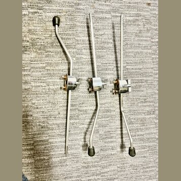 Tři kovové ladicí mechaniky stříbrné barvy s černými knoflíky. Jsou umístěny vedle sebe na šedém texturovaném povrchu. Na součástkách nejsou žádné vi…
