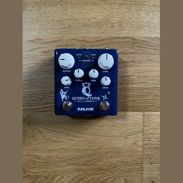Modrý kytarový efekt s bílými ovládacími knoflíky. Na zařízení jsou nápisy SILVER, SHINE, ROUTING, OUTPUT, TREBLE, TONE, LEVEL, GAIN a DRIVE. Ve spod…