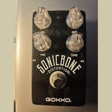 Černý kytarový efekt s čtyřmi průhlednými plastovými knoflíky. Na spodní části je bílý nápis SONICBONE DISTORTION a pod ním značka GOKKO. Nad knoflík…
