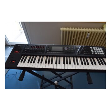 Černý digitální klavír značky Roland s označením RD-64. Na ovládacím panelu jsou nápisy D-BEAM, SOUND MODIFY a ARYTHMIA. Nástroj je umístěn na černém…