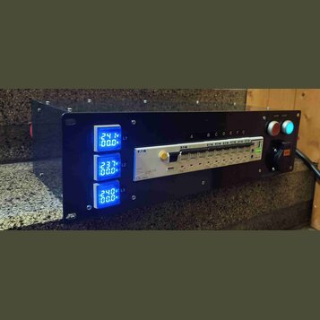 Černý rackový distribuční panel s třemi modrými digitálními voltmetry a ampérmetry označenými L1, L2 a L3. Uprostřed je umístěn bílý proudový jistič…
