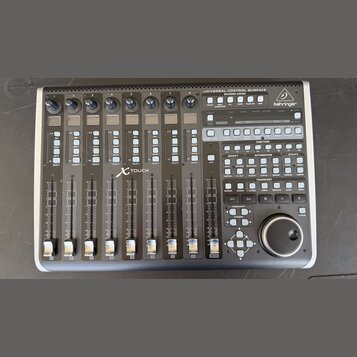 Černá kontrolní plocha s nápisem UNIVERSAL CONTROL SURFACE ENCOVER ROSSIGN a logem behringer. Zařízení obsahuje osm posuvníků, řadu tlačítek s různým…