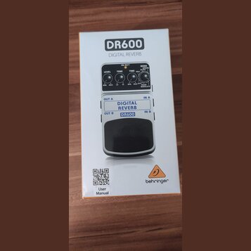 Fotografie znázorňuje krabici od efekt pedálu. Na krabici je zobrazen přístroj s nápisy DR600 DIGITAL REVERB a logo behringer. Na obrázku pedálu jsou…