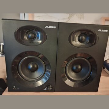 Dva černé studiové monitory s logem Alesis v pravém horním rohu. Každý reproduktor obsahuje jeden výšký a jeden basový měnič. Na levém monitoru jsou…