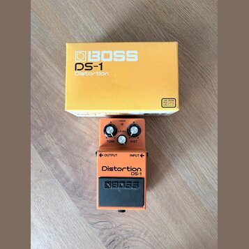 Oranžový efekt pedál s černým spodním panelem a stříbrnými ovládacími knoflíky. Na pedálu jsou nápisy CHECK, LEVEL, TONE, DIST, OUTPUT, INPUT, Distor…