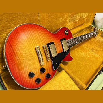Elektrická kytara s trupem ve tvaru single-cut a povrchem v červeno-žlutém přechodu (sunburst) s viditnou strukturou dřeva. Nástroj má dva humbuckery…