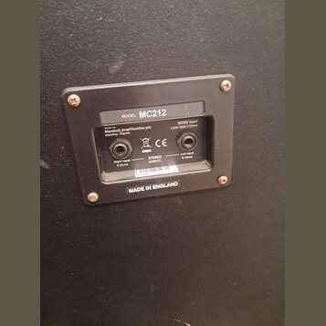 Fotografie zachycuje zadní panel reproduktoru s černým povrchem. Na stříbrném štítku je uveden nápis MODEL: MC212, made by Marshall Amplification plc…