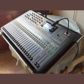 Digitální mixážní pult stříbrné barvy s velkým množstvím posuvníků, tlačítek a otočných ovladačů. Na pravé straně je vidět logo Soundcraft a název mo…