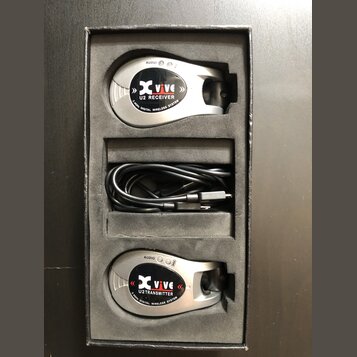 V černé krabičce s pěnovou vložkou jsou umístěny dvě stříbrné bezdrátové jednotky a černý USB kabel. Horní jednotka nese nápisy Xvive, U2 RECEIVER a…