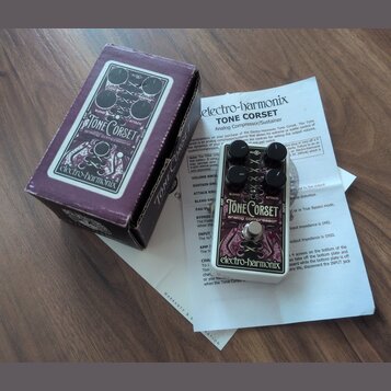 Na fotografii je efekt pedál Electro-Harmonix Tone Corset v bílém provedení s černými ovládacími prvky. Na pedálu jsou nápisy TONE Corset, analog com…