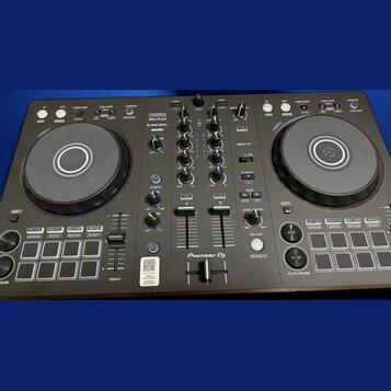 Černý DJ kontrolér s dvěma jog-koly a středovým mixážním sekcí. Na zařízení jsou viditelné nápisy DDJ-FLX4, rekordbox a serato, v dolní části je logo…