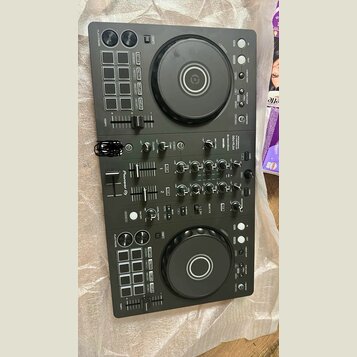 Černý DJ kontrolér s dvěma velkými jog-koly astředovými tlačítky. Na přístroji je vidět nápis Pioneer DJ a označení modelu DDJ-FLX4. Povrch obsahuje…