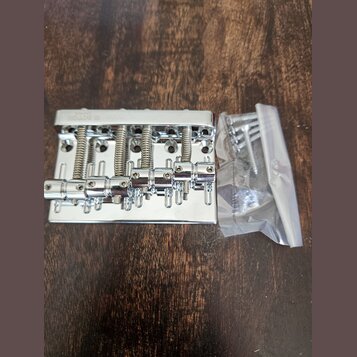 Stříbrný kovový kobylník na elektrickou kytaru s pěti sedly a odpružineným mechanismem. Na horní hraně je vyryt nápis GOTOH JAPAN. Vedle nástroje se…