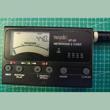 Černý digitální metronom a ladička s LCD displejem. Na přístroji je bílý nápis musedo MT-80 METRONOME & TUNER a označení MIC. Displej zobrazuje hodno…