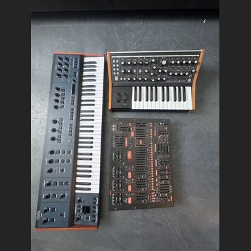 Fotografie zobrazuje tři elektronické hudební přístroje. Vlevo je šedý syntetizátor s klaviaturou a nápisem UMIKKO v levém dolním rohu. Vpravo nahoře…
