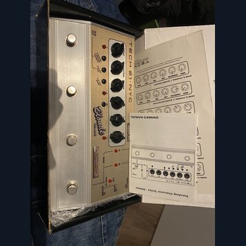 Kremové kytarové pedály v hliníkovém šasi s nápisy TECH 21 NYC, SansAmp a Blonde DELUXE. Zařízení má pět otočných ovladačů s popisky DRIVE, CHARACTER…