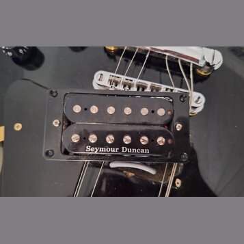 Černý humbucker s dvěma řadami snímacích pólů, umístěný v černém plastovém rámečku na černé kytare. Na spodní části snímače je bílý nápis Seymour Dun…