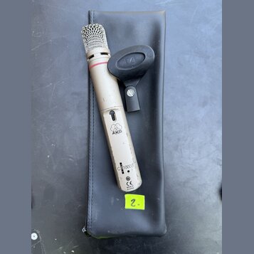 Kondenzátorový mikrofon stříbrné barvy s kovovou síťkou v horní části a červeným prstenem pod ní. Na těle je viditelné logo AKG, nápis C1000 S a ozna…