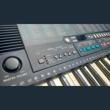 Detailní pohled na ovládací panel a klávesy elektronického klavíru. Na panelu jsou nápisy OVERALL CONTROLL, TEMPO, TRANSPOSE a SPLIT POINT CHANGE. V…