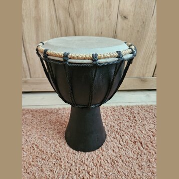 Černý djembe s hrací plochou z pleti v přirozené světlé barvě. Horní okraj je opleten kombinací černého a béžového provázku. Na těle nástroje nejsou…