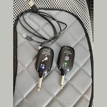 Dva černé bezdrátové vysílače s kovovými konektory typu jack. Na levém je nápis „A8 Original sound Transmitter“ a symbol klíče, na pravém „A8 Origina…