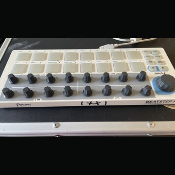 Bílý MIDI kontrolér s názvy Arturia a BEATSTEP Controller & Sequencer. Zařízení obsahuje dvě řady bílých čtvercových padů, 16 černých otočných knoflí…