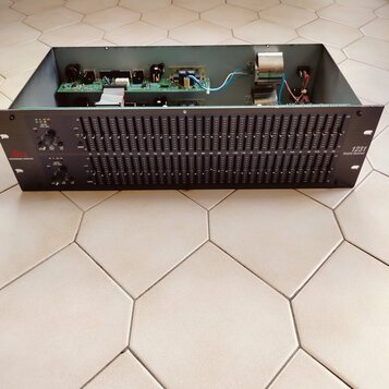 Černý rackový grafický ekvalizér s řadou posuvníků. Na levé straně je logo dbx PROFESSIONAL PRODUCTS a na pravé straně nápis 1231 Graphic Equalizer.…
