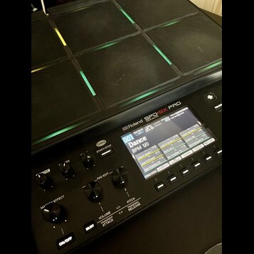 Černý sampling pad značky Roland s nápisem SPD-SX PRO. Zařízení má mřížku gumových padů s podsvícením v různých barvách. Displej zobrazuje název „001…