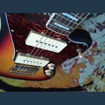 Detail elektrické kytary s barevným přechodem těla od červené přes oranžovou k žluté. Nástroj má tmavě červenou zrcadlovou pickguard s dvěma bílými s…