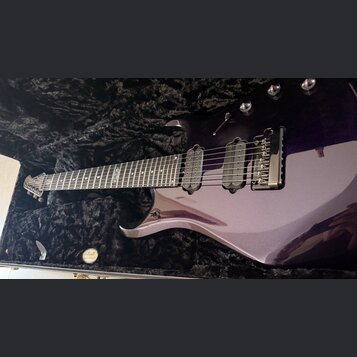 Fialová elektrická kytara v černém polstrovaném kufru. Na hmatníku je viditelný nápis "Custom Shop". Kytara má dva snímače typu humbucker a fixní mos…