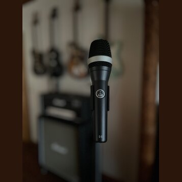 Černý dynamický mikrofon s mřížkou a bílým prstenem v horní části. Na těle je viditelné logo AKG a nápis D 5. Povrch mikrofonu je matný a v dobrém st…