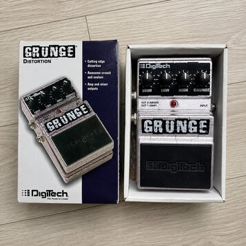 Fotografie zobrazuje efekt pedál v originální krabici. Na pedálu i na krabici je výrazný nápis GRUNGE a logo DigiTech. Zařízení má stříbrný kovový po…