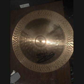 Kruhový činel z mosazného kovu s výrazným žebrováním v centrální části a kováními (důlky) po celém okraji. Na povrchu je černé logo Paiste a nad ním…